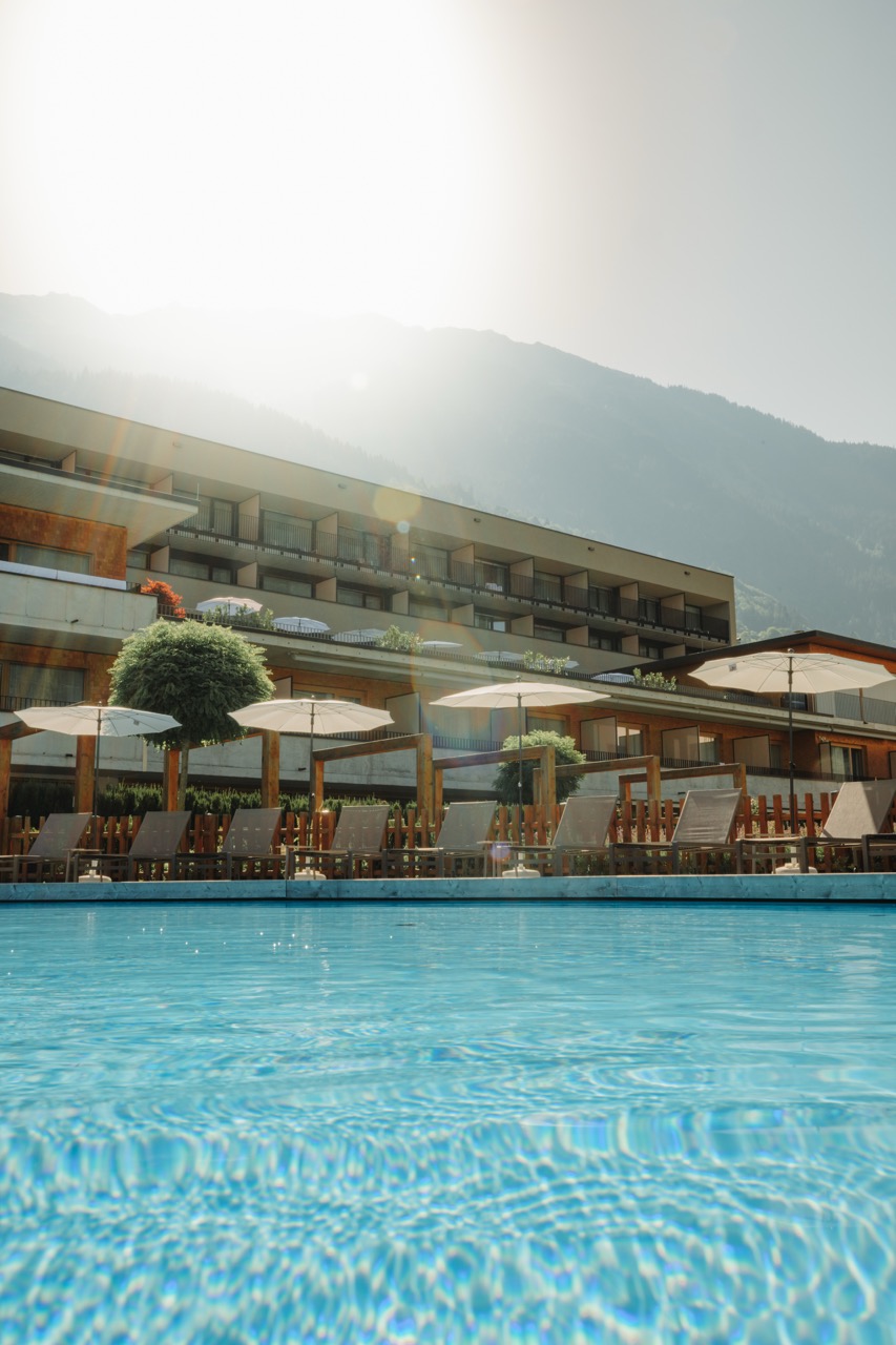 Hotelpool mit Sonnenschirmen und Bergpanorama im Gegenlicht
