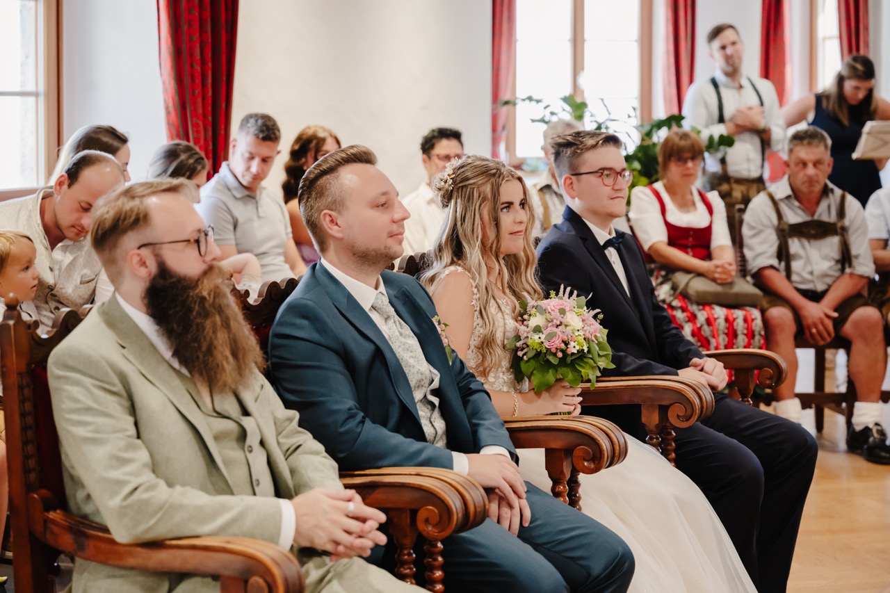 Brautpaar und Gäste sitzen bei der standesamtlichen Trauung in festlichem Saal